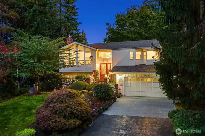 Nestled in a lush, park-like setting, this beautifully maintained home shines with warm evening glow and timeless curb appeal. Expansive picture windows flood the interior with natural light, while vaulted ceilings and a striking mid-century flair add a sense of openness and style. Mature landscaping frames the entry, creating a private oasis just minutes from town conveniences. Enjoy the inviting front porch, spacious driveway, and beautifully lit architectural lines that highlight the home’s welcoming character. Ideal for those who appreciate serenity, space, and thoughtful design in a prime location! ????