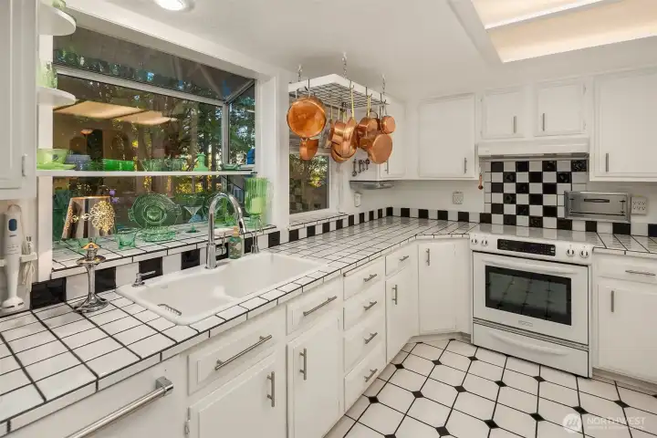 This cheerful kitchen offers a timeless black-and-white design with abundant counter space and cabinetry. A large garden window frames serene treetop views while flooding the space with natural light—perfect for morning coffee or preparing meals with ease.