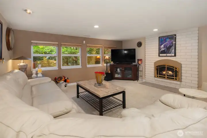 Spacious and inviting, this lower-level family room offers the perfect retreat for movie nights or casual gatherings. A wall of windows brings in lush garden views and natural light, while the cozy brick fireplace with elegant gold trim creates a warm focal point. The open layout easily accommodates a sectional and media setup—ideal for relaxation, entertaining, or creating a multi-use space. ????