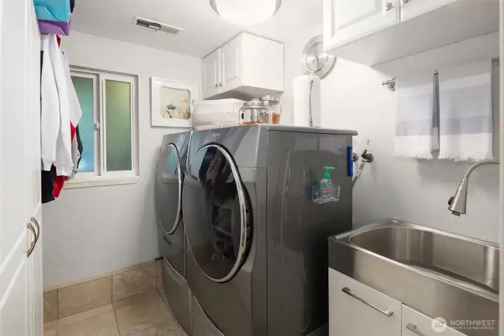 Efficient and thoughtfully designed laundry room featuring a modern front-load washer and dryer, built-in cabinetry for storage, and a convenient utility sink. Tile floors and updated lighting add a clean, polished touch, making this space as functional as it is stylish. A bright, organized area that keeps household tasks simple and seamless. ???