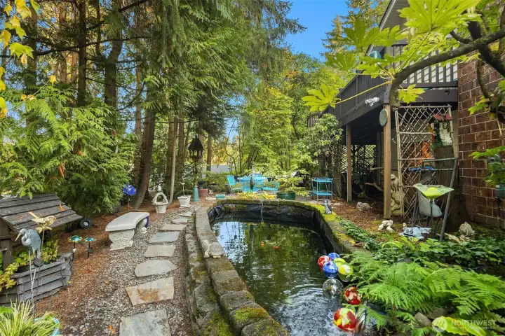 A tranquil backyard escape featuring a stone path, mature trees, and a soothing pond. The natural landscaping and shade canopy create a true woodland retreat.