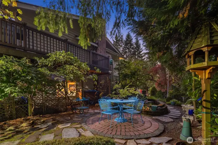 Lush landscaping surrounds the brick patio, blending vibrant greenery with colorful planters. A serene, fenced setting ideal for morning coffee or a relaxing evening.