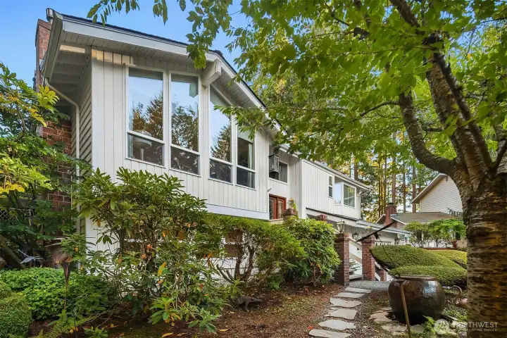 Welcoming stone walkway leads to a charming entry framed by greenery. Oversized front windows fill the home with natural light and showcase its mid-century-inspired design.