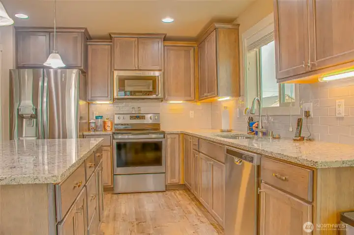 KITCHEN FEATURES: Granite Countertops, LVP Flooring, Under-Cabinet Lighting, Stainless Steel Appliances including LG Refrigerator and Whirlpool Range/Oven & Dishwasher, KitchenAid Microwave/Convection Combo, Stainless Steel Divided Sink with Garbage Disposal, Culligan Water Filtration System, and Kitchen Island with Seating and Added Cabinet Storage.