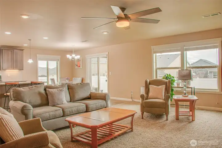DINING SPACE & BACKYARD ENTRY FROM MAIN ROOM: Carpeted, Ceiling Fan, East- and South-Facing Windows with 2" Horizontal Vinyl Blinds, Sliding Glass Door with Vertical Blinds; Kitchen Under-Cabinet Lighting Also Visible
