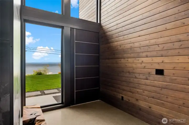 Welcoming entry with modern door and warm wood accents, framed by large windows and serene water views.