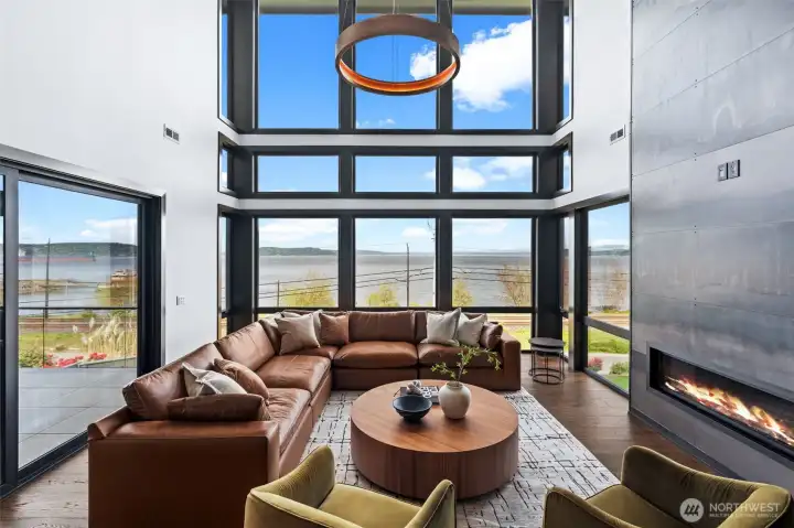 The living area features soaring ceilings, floor-to-ceiling windows, and stunning water views.