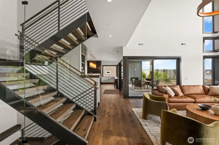 Open living area with striking staircase, warm wood floors, and easy flow to kitchen and covered outdoor space with water views.
