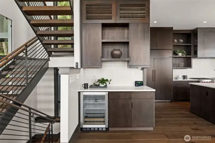 Built-in beverage area with custom cabinetry, wine fridge, and open shelving, conveniently located near kitchen and living spaces.