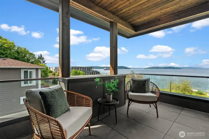 Upper-level covered deck with glass railing, offering sweeping views of the water and Ruston.