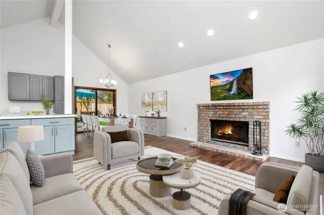 Living room with vaulted ceilings, abundance of natural light with wall of windows & wood burning fireplace.