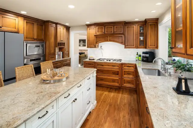 A stunning, remodeled Gourmet Kitchen with a large granite island/eating bar & stunning custom cabinets, stainless steel Dacor & Meile appliances including a 5-burner gas cooktop with a pot filler, under-cabinet lighting, planning desk space, dove-tailed wood, quiet-close drawers, subway tile backsplash, and a garden window overlooking the back yard.