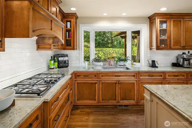 A stunning, remodeled Gourmet Kitchen with a large granite island/eating bar & stunning custom cabinets, stainless steel Dacor & Meile appliances including a 5-burner gas cooktop with a pot filler, under-cabinet lighting, planning desk space, dove-tailed wood, quiet-close drawers, subway tile backsplash, and a garden window overlooking the back yard.