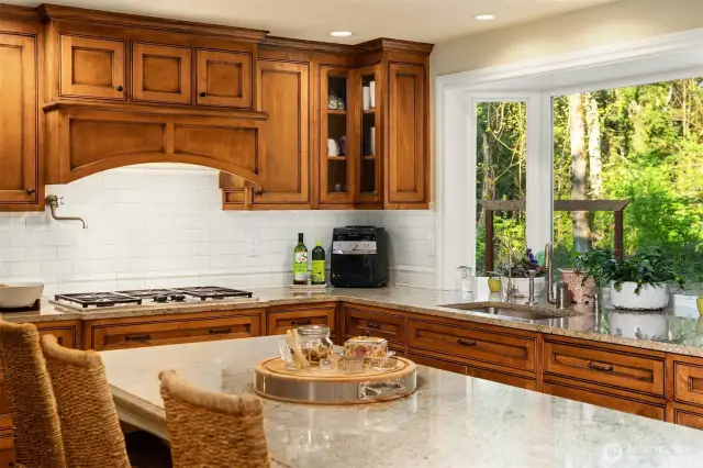 A stunning, remodeled Gourmet Kitchen with a large granite island/eating bar & stunning custom cabinets, stainless steel Dacor & Meile appliances including a 5-burner gas cooktop with a pot filler, under-cabinet lighting, planning desk space, dove-tailed wood, quiet-close drawers, subway tile backsplash, and a garden window overlooking the back yard.