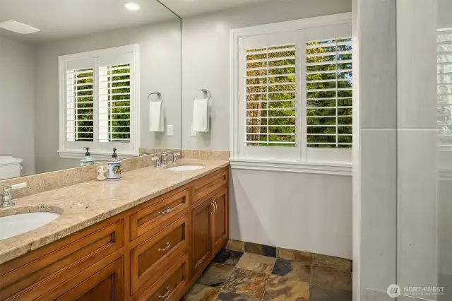 The updated main/guest 3/4 bathroom with a dual vanity, granite counters, slate tile floors and tile shower with a rain showerhead.