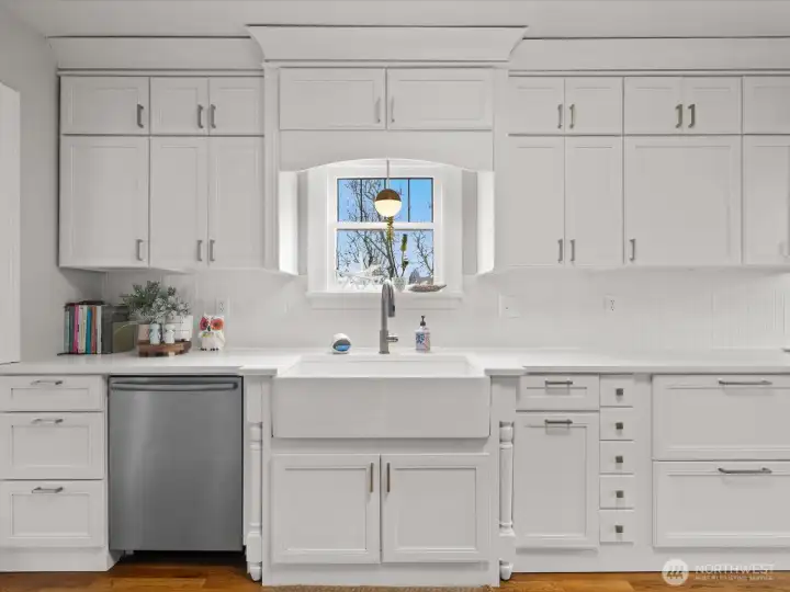 The kitchen impresses with its all-white cabinetry, farmhouse sink, and sleek appliances