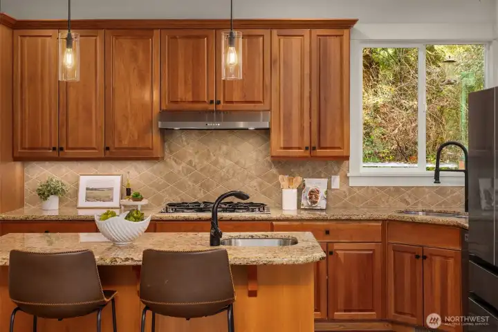 Open kitchen with abundant cabinetry, granite counters, gas range, and island with seating for casual dining.