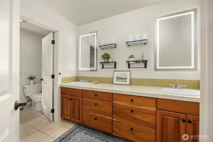 Spacious bathroom featuring double sinks, generous cabinetry, and private toilet area and tub/shower room.