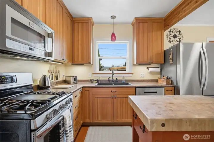 There is a stainless steel 5-burner gas range with a microwave above, and a stainless dishwasher and French door refrigerator.