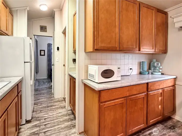 More kitchen storage on the right just past the microwave. Beyond that is the bathroom (on the right), addition access on the left behind the refrigerator, and the bedroom at the end of the hall.