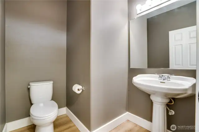 The powder room has been elegantly refreshed with a new toilet, updated trim, fresh paint, and a stylish pedestal sink, adding a touch of sophistication to the main floor.