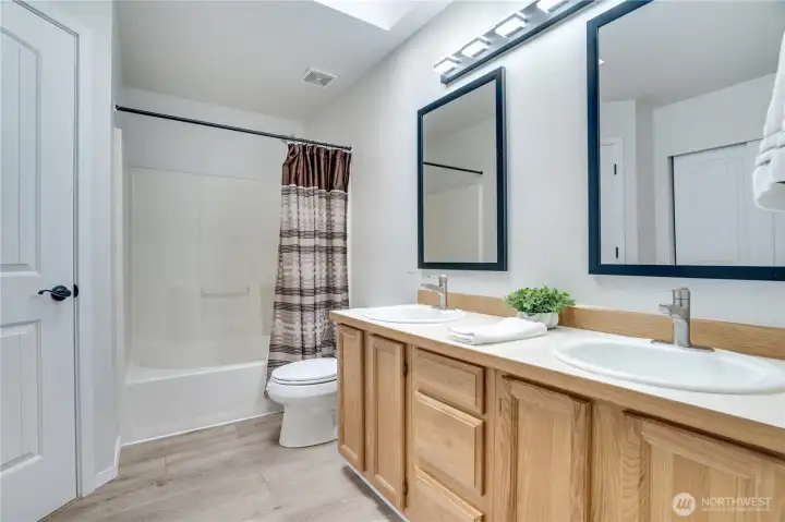 Primary bathroom with laminate floors, double vanity with newer mirror and light fixture, skylight and walk-in closet through the door on the left.