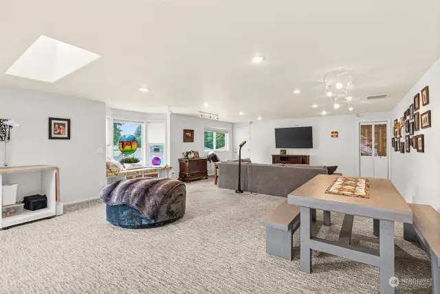 This large gathering media room is perfect for movie nights, gaming, and crafting activities, offering a versatile space for family and friends. A bay window fills the room with natural light and provides a cozy nook for reading or relaxing, while a skylight enhances the airy, open feel. A sliding glass door opens to a deck, ideal for outdoor lounging, and a nearby door leads directly to the inground pool area, creating easy access for poolside fun and entertainment. The room's layout makes it a great hub for both indoor and outdoor activities.            This large gathering media room is perfect for movie nights, gaming, and crafting activities, offering a versatile space for family and friends. A bay window fills the room with natural light and provides a cozy nook for reading or relaxing, while a skylight enhances the airy, open feel. A sliding glass door opens to a deck, ideal for outdoor lounging, and a nearby door leads directly to the inground pool area.