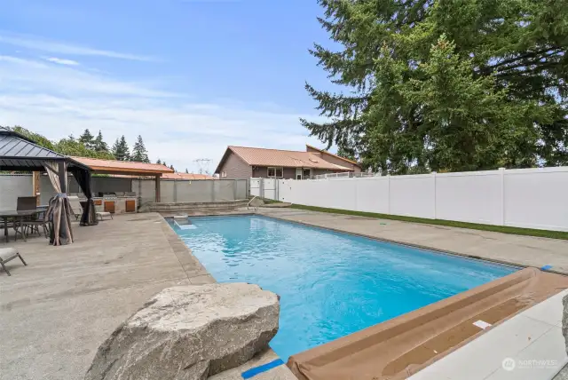 16x40 inground heated pool is surrounded by exposed aggregate and bordered by maintenance-free ForeverLawn Astroturf for a clean, soft finish. Equipped with a robot pool cleaner and skimmer, it offers effortless upkeep, while a  pool cover ensures year-round care. Fully fenced for complete privacy.