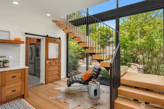 A dramatic architectural staircase rises against a wall of windows, framing views of the lush garden retreat and inviting the outdoors in.