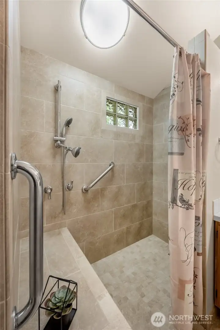 Oversized walk-in tile shower with grab bars and seating bench for comfort and ease.