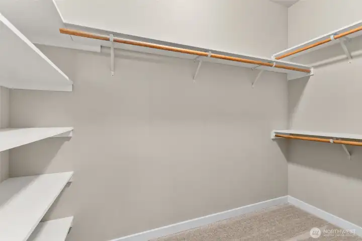 Primary walk-in closet boasts of hanging space and solid wood shelving.