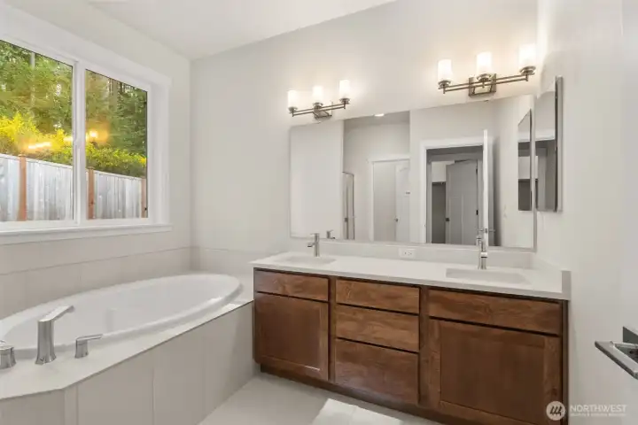 Primary bathroom has a double vanity with undermount dual sinks, tile floor, quartz countertops and a soaking tub with tile surround.