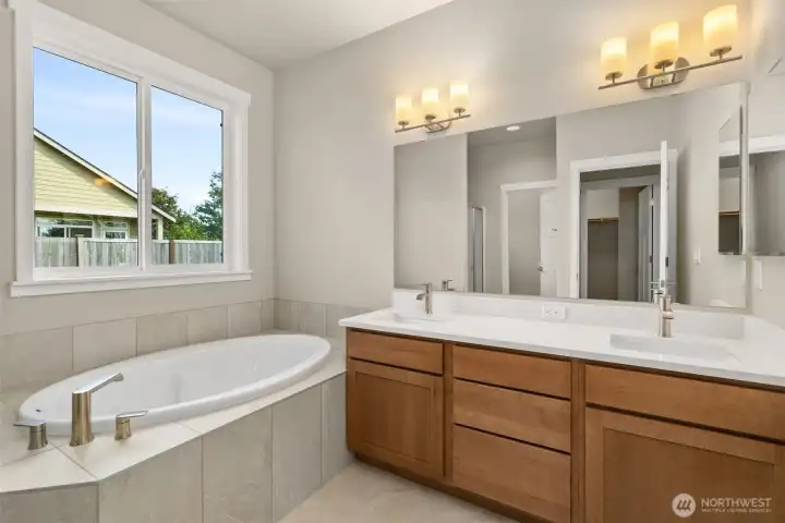 Primary bathroom has a double vanity with undermount dual sinks, tile floor, quartz countertops and a soaking tub with tile surround.