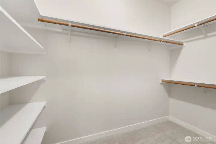 Primary walk-in closet boasts of hanging space and solid wood shelving.