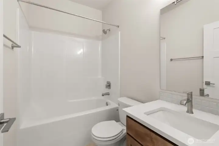 Full bathroom with undermount sink in Toffee-stained Maple cabinetry, quartz countertop with backsplash and tub/shower combo.