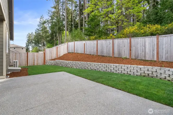 Spacious patio and lush lawn framed by a tiered retaining wall and wooded backdrop.