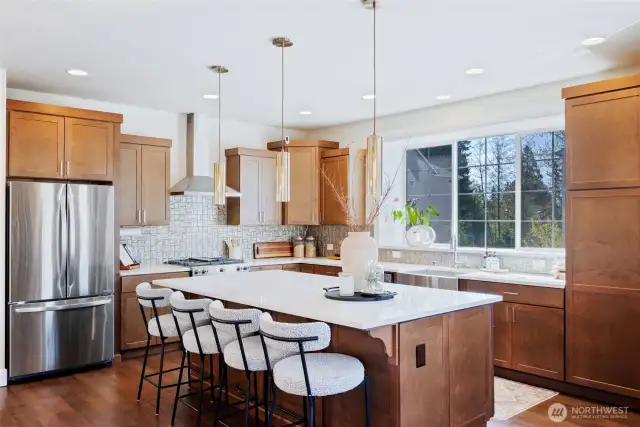 Chef-inspired kitchen with quartz countertops, a generous island, designer pendants, stainless steel appliances, rich cabinetry and a large window.