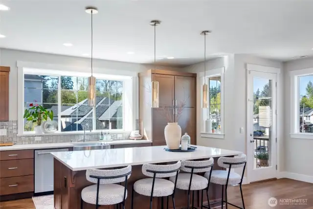 Chef-inspired kitchen with quartz countertops, a generous island, designer pendants, stainless steel appliances, rich cabinetry and a large window.
