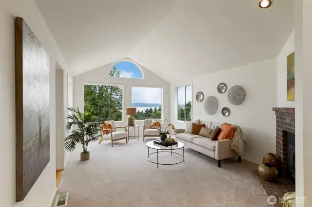 Soaring ceilings and oversized windows frame serene water views in this airy, light-filled living room. The space is anchored by a classic brick fireplace and designed for both relaxing and entertaining.