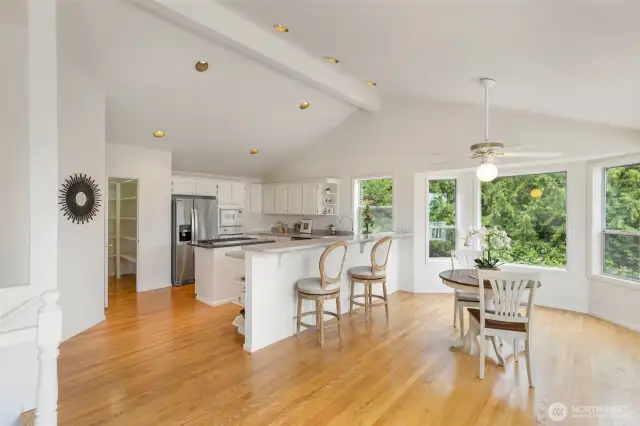 Light, bright, and perfectly functional, this open-concept kitchen features white cabinetry, a spacious peninsula with seating, and a sunny dining nook surrounded by windows that bring the outdoors in.