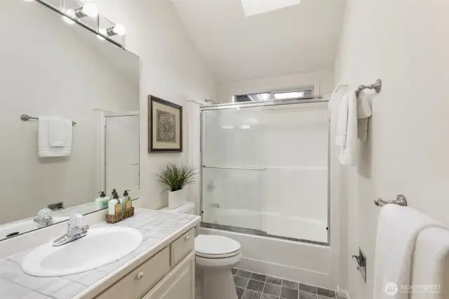 Bright and clean full bathroom featuring a skylight, tile countertop, and a tub/shower combo with sliding glass doors.
