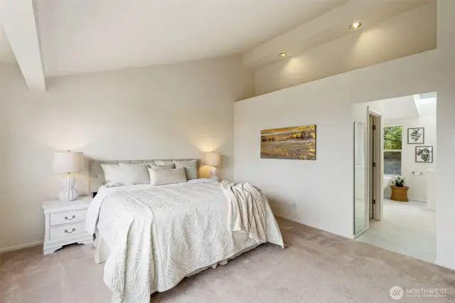 Spacious primary bedroom with vaulted ceilings, soft neutral tones, and an airy layout. Recessed lighting and natural light enhance the peaceful atmosphere.