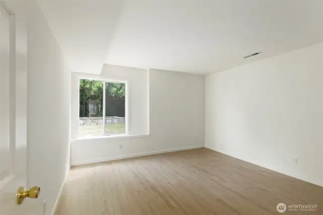 Bright and versatile lower-level bedroom with new flooring, a large window, and a simple layout offering plenty of space to personalize.
