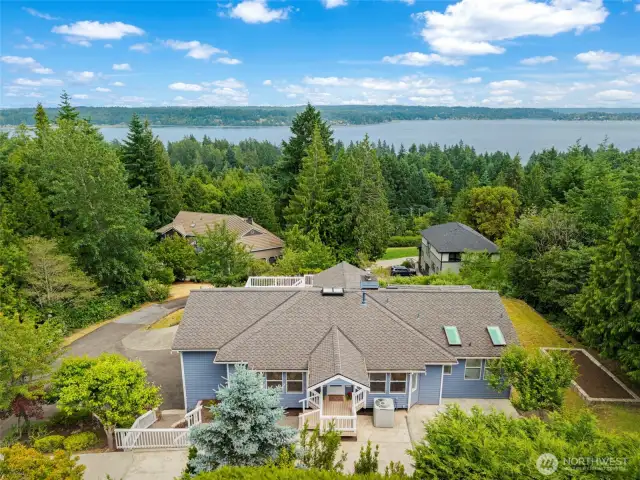 An aerial view highlights the home's incredible vantage point overlooking the shimmering waters of the Puget Sound. Surrounded by evergreens, this home offers peace and privacy in a stunning natural setting.