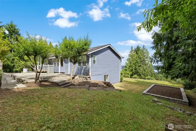 The side yard includes tiered patios and garden beds with space for outdoor dining, gathering, or planting.