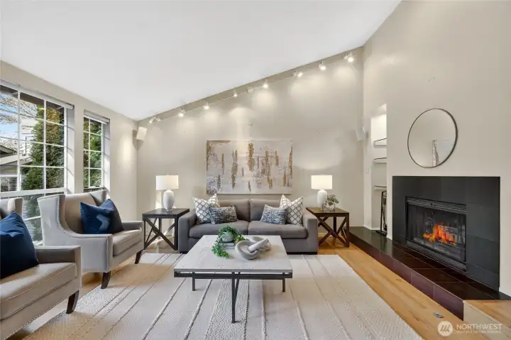 Light-filled living room with soaring ceilings, fireplace & large windows. Stylish finishes, hardwood floors & open layout create a warm, inviting space.