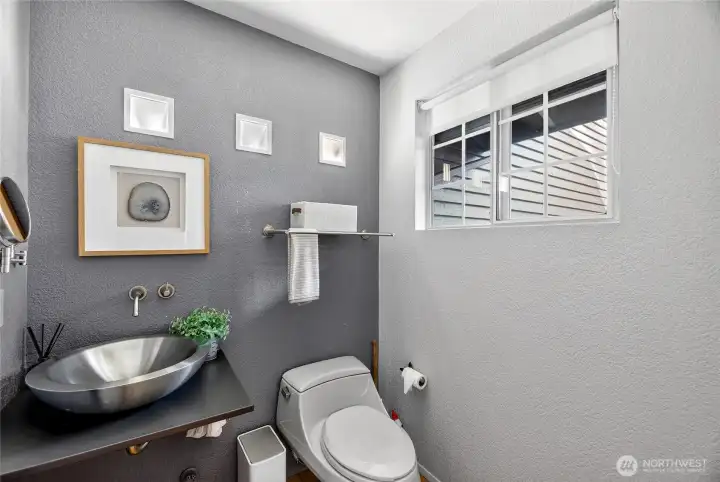 Stylish powder room with modern vessel sink, sleek finishes & designer touches. Window brings in natural light, creating a bright, refreshed feel.