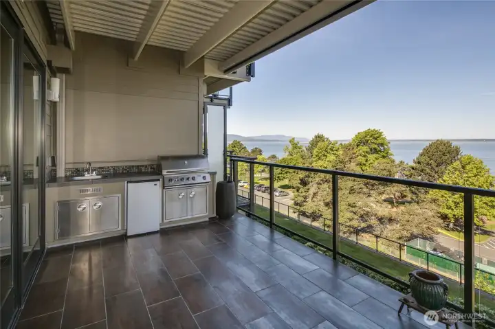 Looking toward the South end of the deck to the outdoor kitchen with a gas grill, small refrigerator and stainless sink, with additional storage space below.