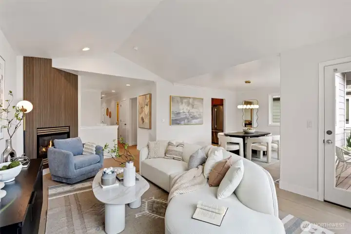 The spacious living room sports vaulted ceilings, vinyl plank flooring and a cozy gas burning fireplace with fluted wood statement wall.