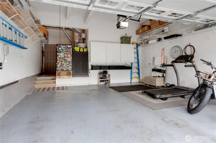 A spotless two car garage has shelving and cabinetry keeping your household items organized.